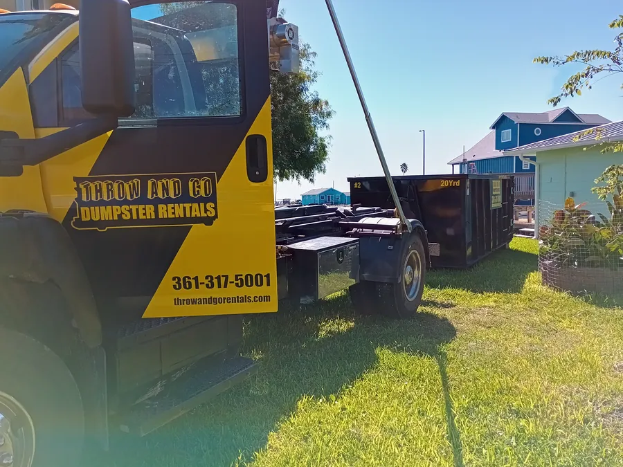 Throw and Go black and yellow roll-off dumpster truck in a Corpus Christi neighborhood